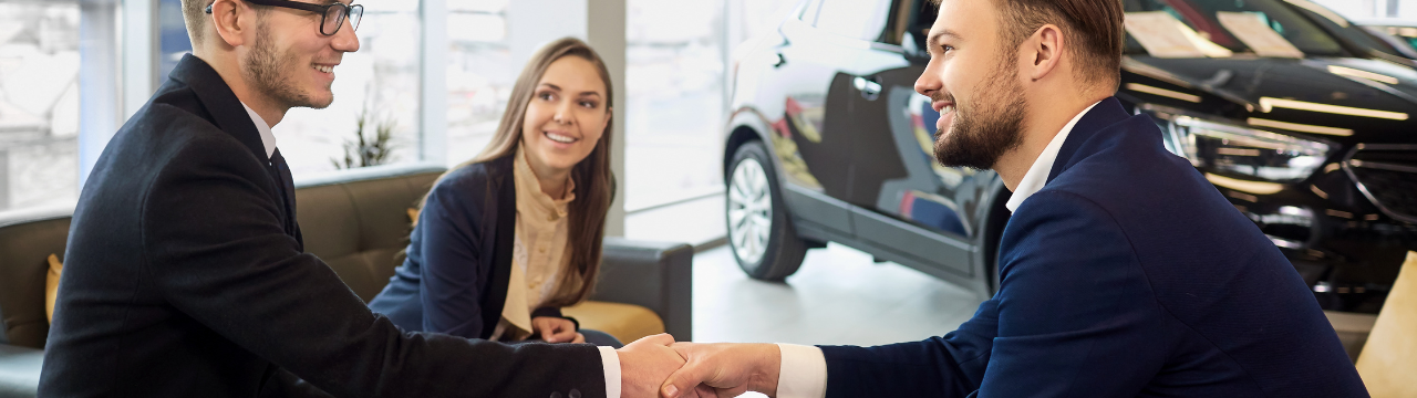 Men shaking hands in car dealership with woman